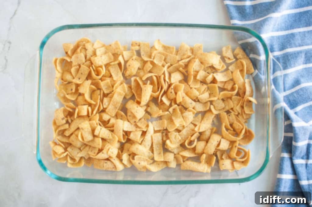 Overhead shot of corn chips arranged in a clear glass baking dish, with a blue striped cloth beside it.