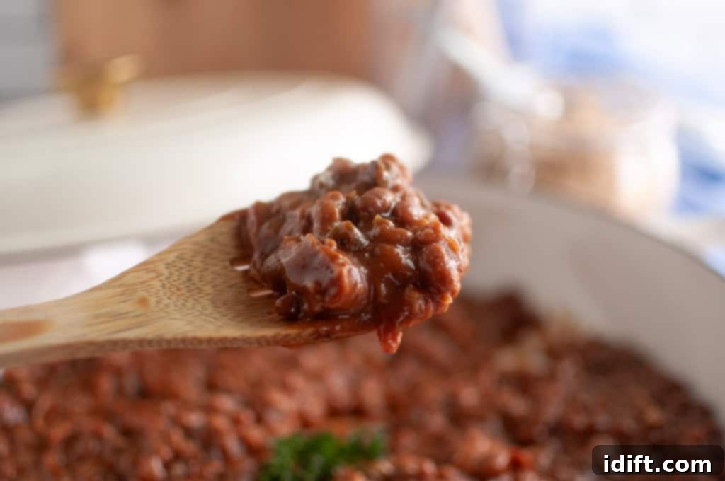 A wooden spoon holds a serving of thick, chunky chili above a pot filled with more chili, ready to be dished out and enjoyed.