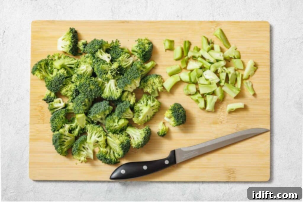 Chopped broccoli florets and stems on a wooden cutting board with a black-handled knife.