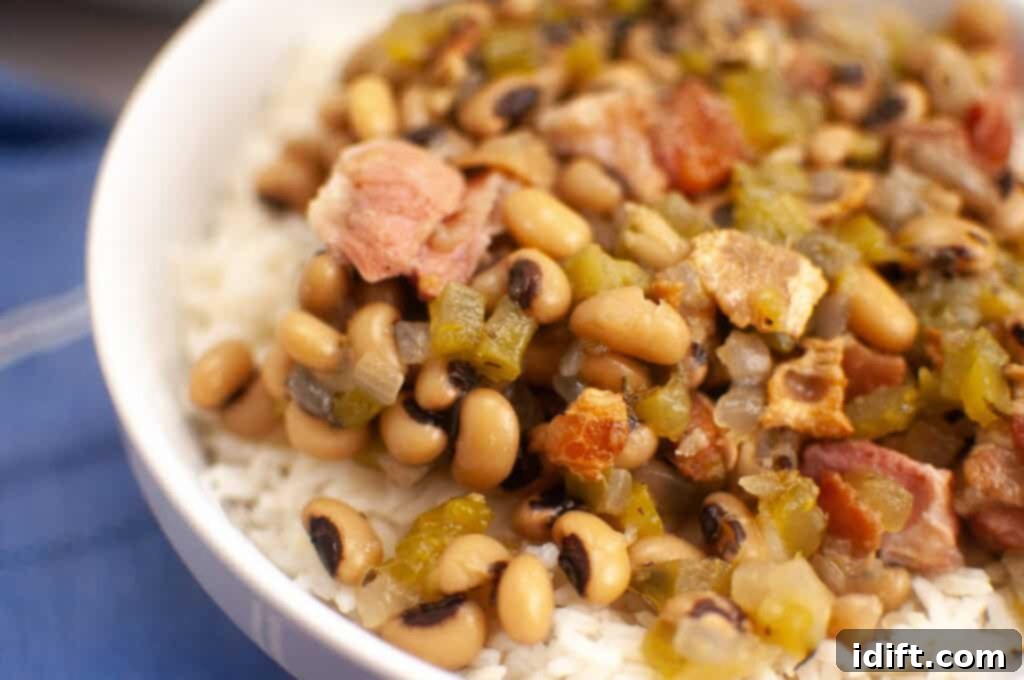 A close-up of a bowl filled with cooked white rice topped with black-eyed peas, diced vegetables, and pieces of meat.