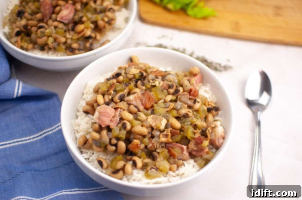 A bowl of rice topped with black-eyed peas, diced ham, and vegetables is placed next to a spoon on a white surface.