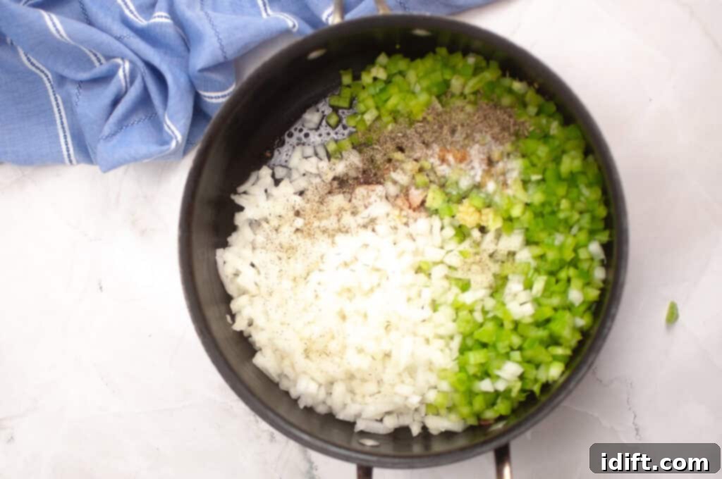 Chopped onions and green bell peppers with seasonings in a saucepan, ready to be cooked, with a blue cloth nearby on a white surface.