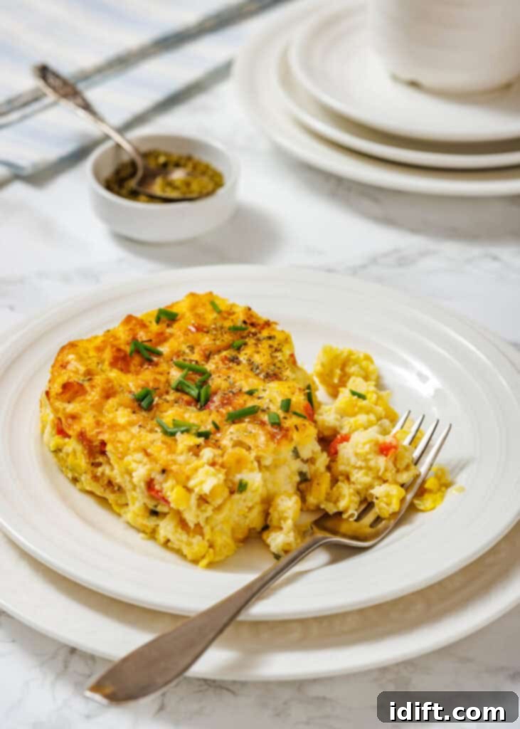 Creamy Golden Corn Bake 2 A serving of corn pudding casserole garnished with chopped chives is on a white plate, with a fork and additional plates in the background.
