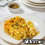 Creamy Golden Corn Bake 11 A serving of corn pudding casserole garnished with chopped chives is on a white plate, with a fork and additional plates in the background.