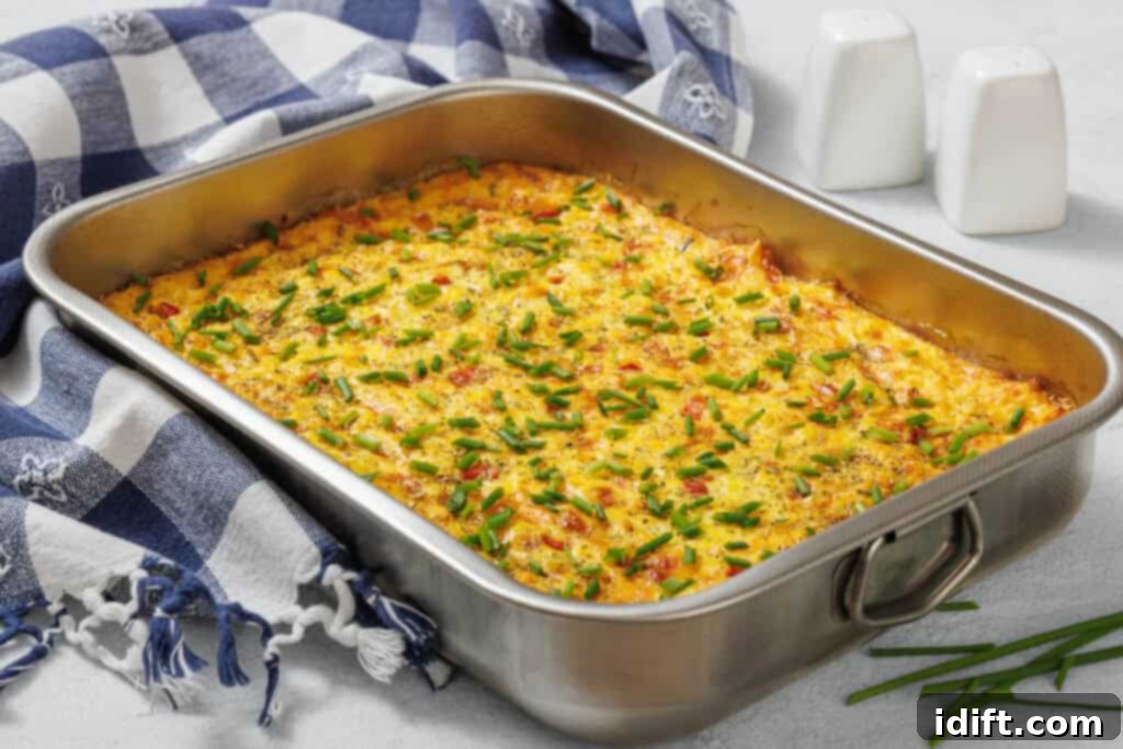 Creamy Golden Corn Bake 9 A corn pudding casserole with chopped chives in a rectangular metal pan, placed on a blue and white checkered cloth next to salt and pepper shakers.