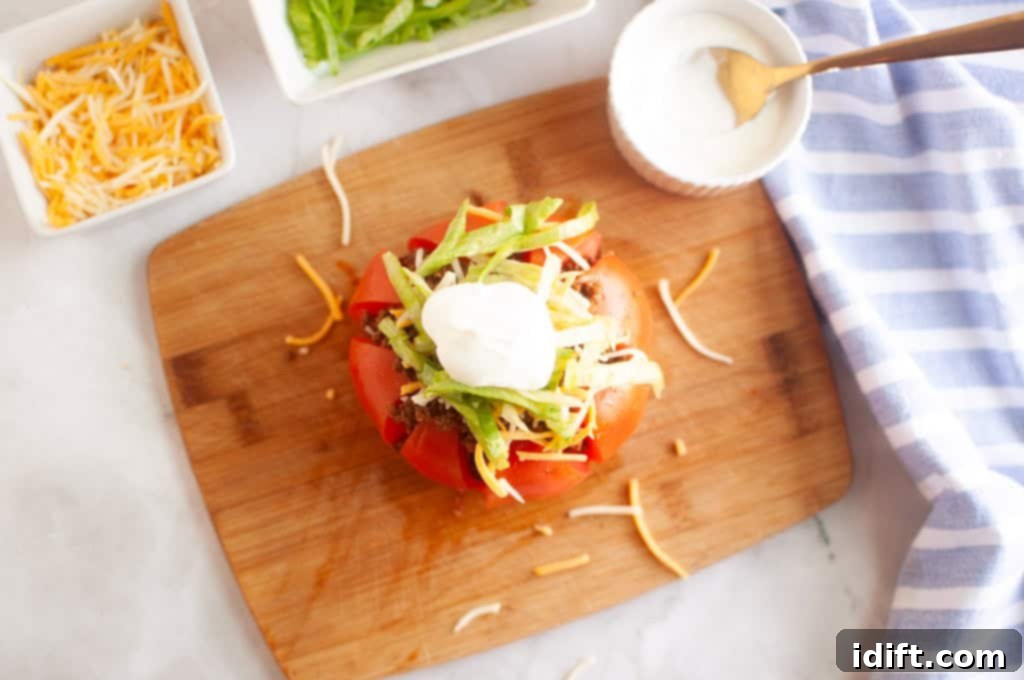 A vibrant, ripe red tomato, hollowed out and overflowing with a rich taco meat filling and various fresh toppings, artfully presented on a crisp white plate.