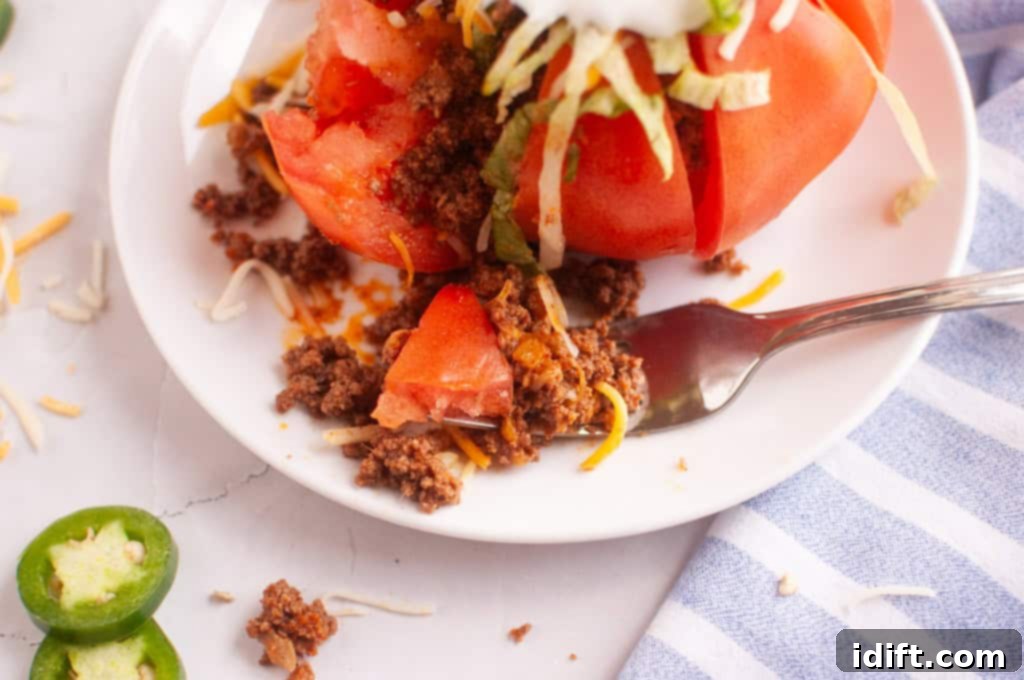 A fork taking a delicious bite out of a vibrant taco stuffed tomato, perfectly presented on a clean white plate.