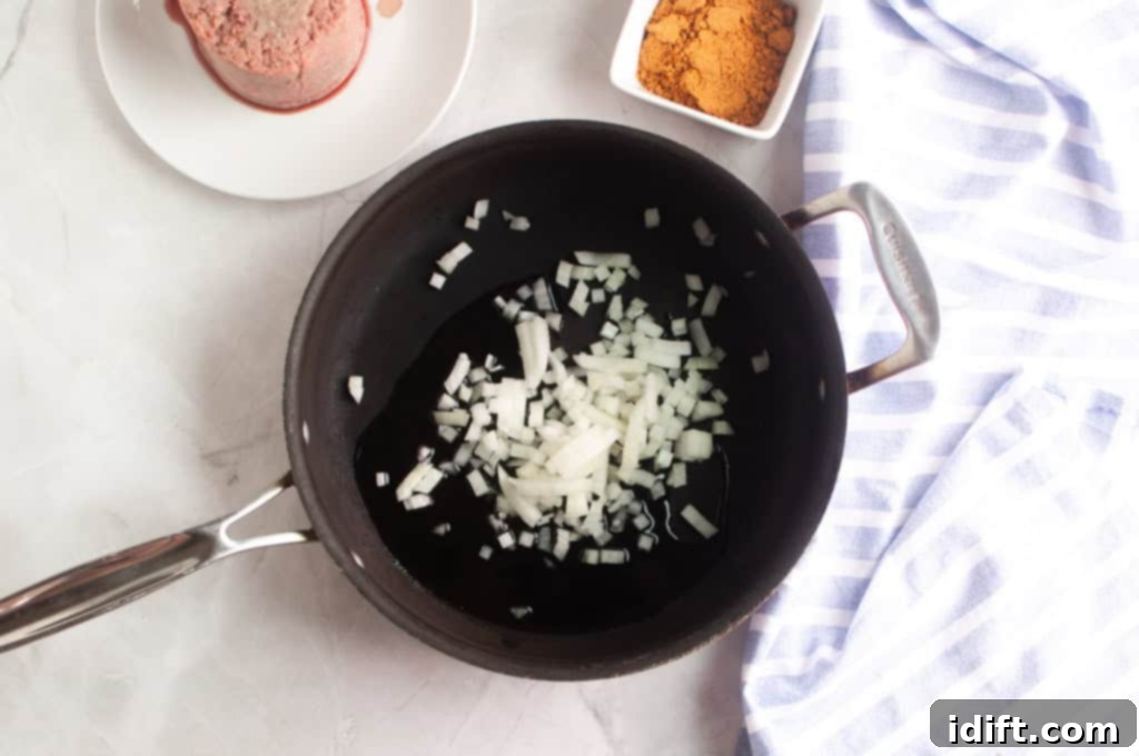 An overhead shot of diced white onions gently sautéing in shimmering olive oil in a black skillet, releasing their sweet aroma.