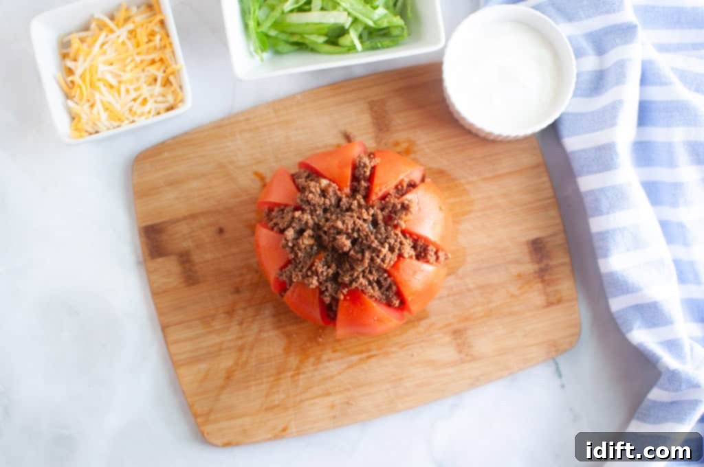 An overhead shot of a ripe tomato being generously filled with savory seasoned ground lamb (beef alternative) on a natural wooden cutting board.