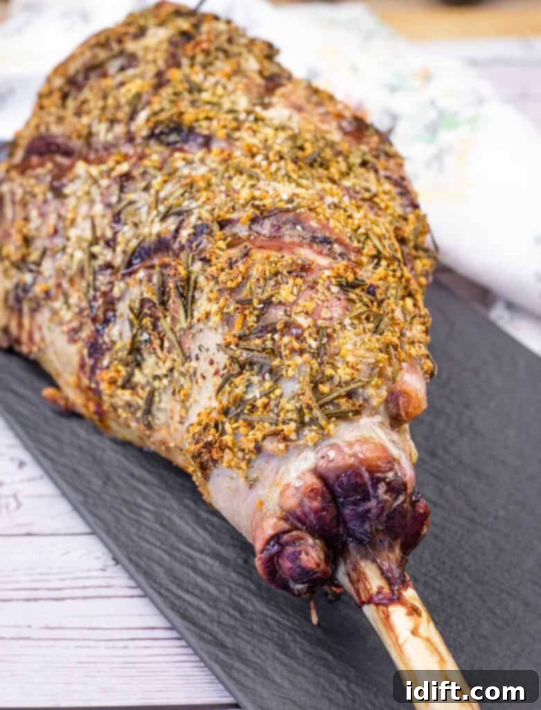 Aromatic Slow-Roasted Lamb Leg 2 A whole roasted leg of lamb seasoned with herbs on a black serving platter, ready to be carved.