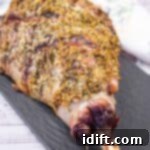 Aromatic Slow-Roasted Lamb Leg 11 A whole roasted leg of lamb seasoned with herbs on a black serving platter.