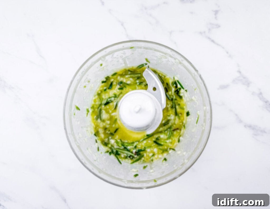 Aromatic Slow-Roasted Lamb Leg 6 Overhead shot of chopped basil, garlic, and olive oil being processed in a food processor, ready for the paste.