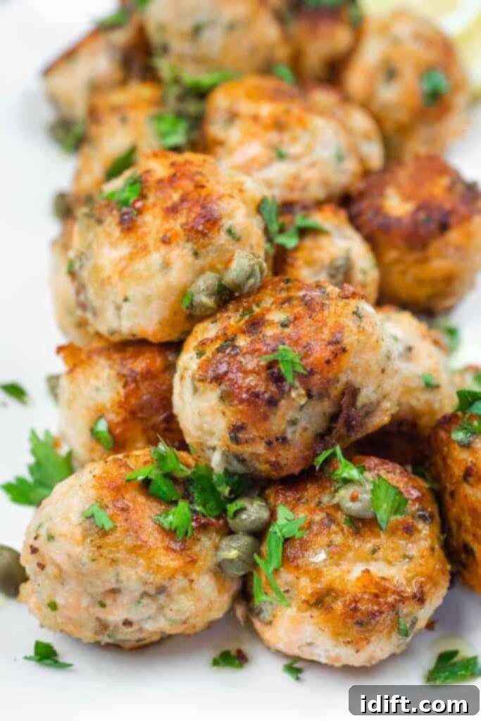 A close-up of a stack of golden-brown salmon balls garnished with fresh capers and vibrant parsley, ready to be served.