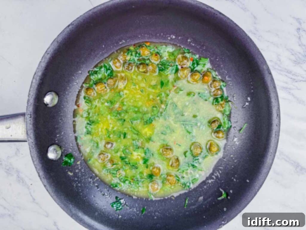 Overhead shot of a luscious lemon-caper sauce, beautifully infused with vibrant fresh parsley, gently simmering in a sleek black pan.