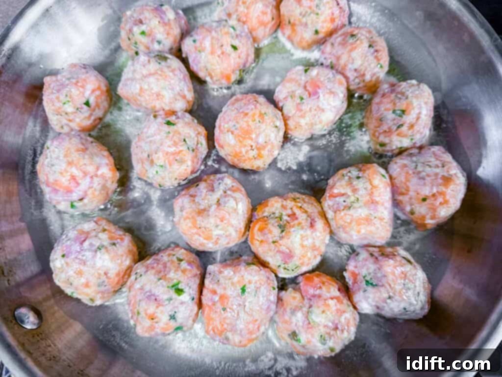 Overhead shot of multiple raw salmon balls sizzling and cooking to golden perfection in a hot pan, demonstrating the pan-frying process.