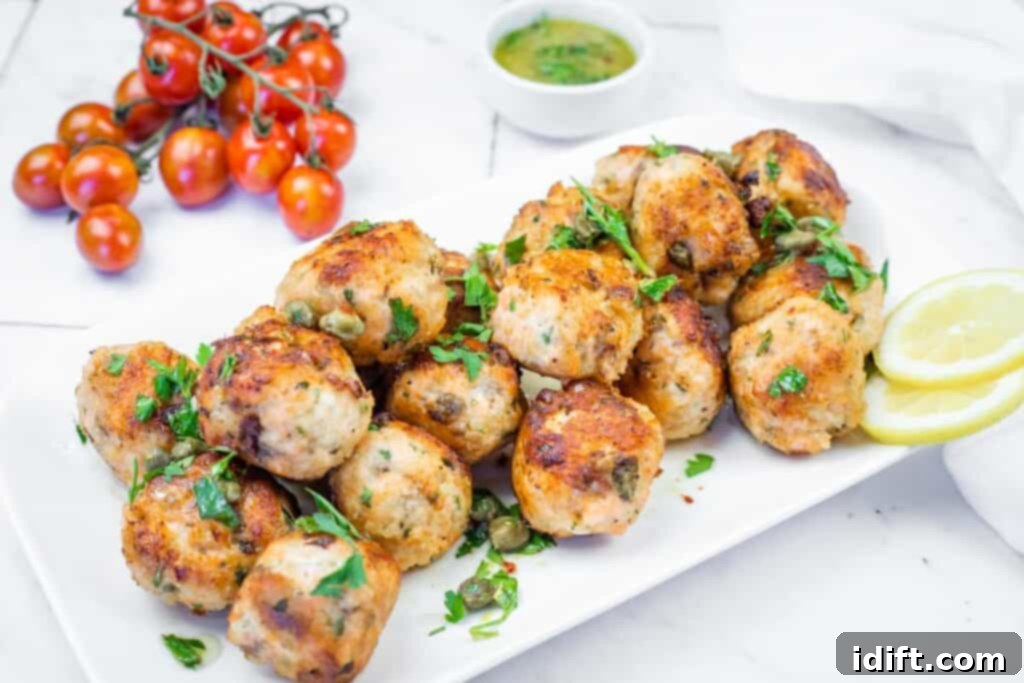 A beautifully presented white platter generously filled with golden-brown salmon meatballs, elegantly garnished with fresh parsley and briny capers, served alongside bright lemon slices and a verdant green sauce.