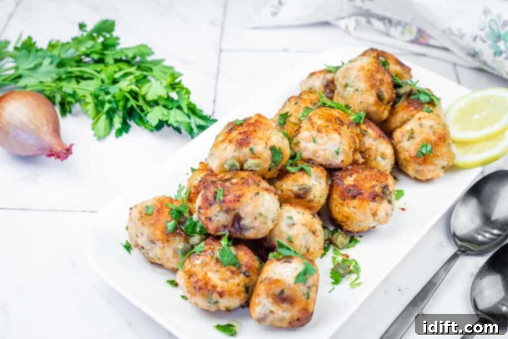 A pristine white platter generously adorned with an array of golden-brown salmon meatballs, elegantly garnished with fresh parsley and briny capers, presented alongside bright lemon slices and decorative spoons, ready for serving.