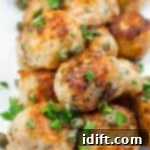 A close-up of a stack of golden-brown salmon meatballs garnished with capers and fresh parsley, looking delicious and ready to be served.