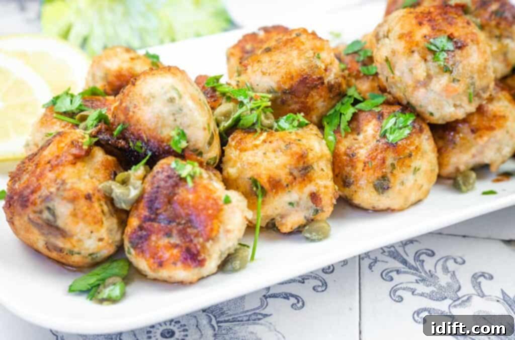 A beautifully arranged white platter showcasing golden-brown salmon balls, artfully garnished with vibrant capers and fresh parsley, with bright lemon slices in the background.