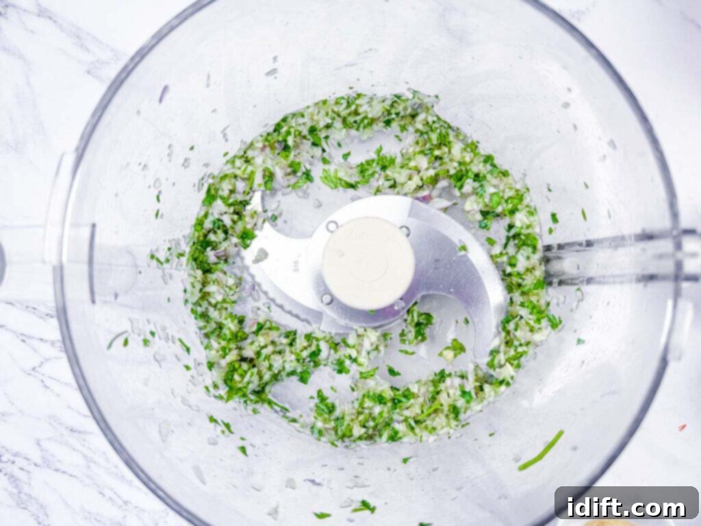 Overhead shot of fresh parsley and shallots being finely processed in a food processor, ready to be incorporated into the salmon mixture.