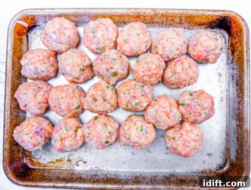 Overhead shot of neatly arranged rows of raw salmon mixture, perfectly formed into uniform 1.5-inch diameter balls, resting on a greased metal baking sheet, ready for chilling.