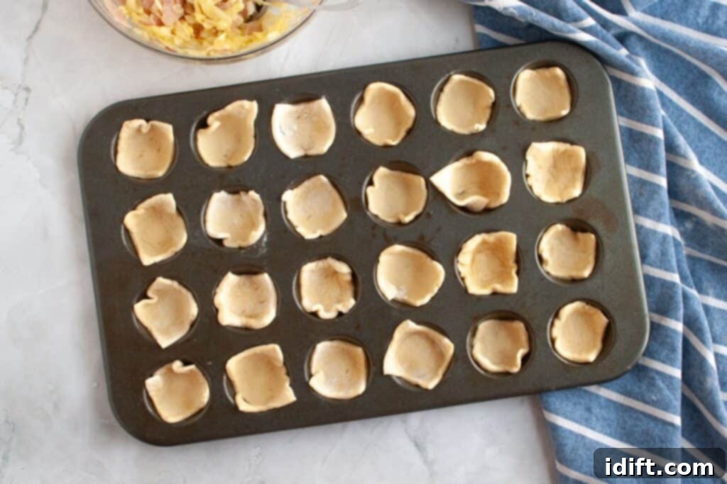 Fluffy Ham and Cheese Bites 8 Overhead shot of a mini muffin tin, with each cup neatly lined with a small piece of crescent dough, forming a pastry shell ready for filling.
