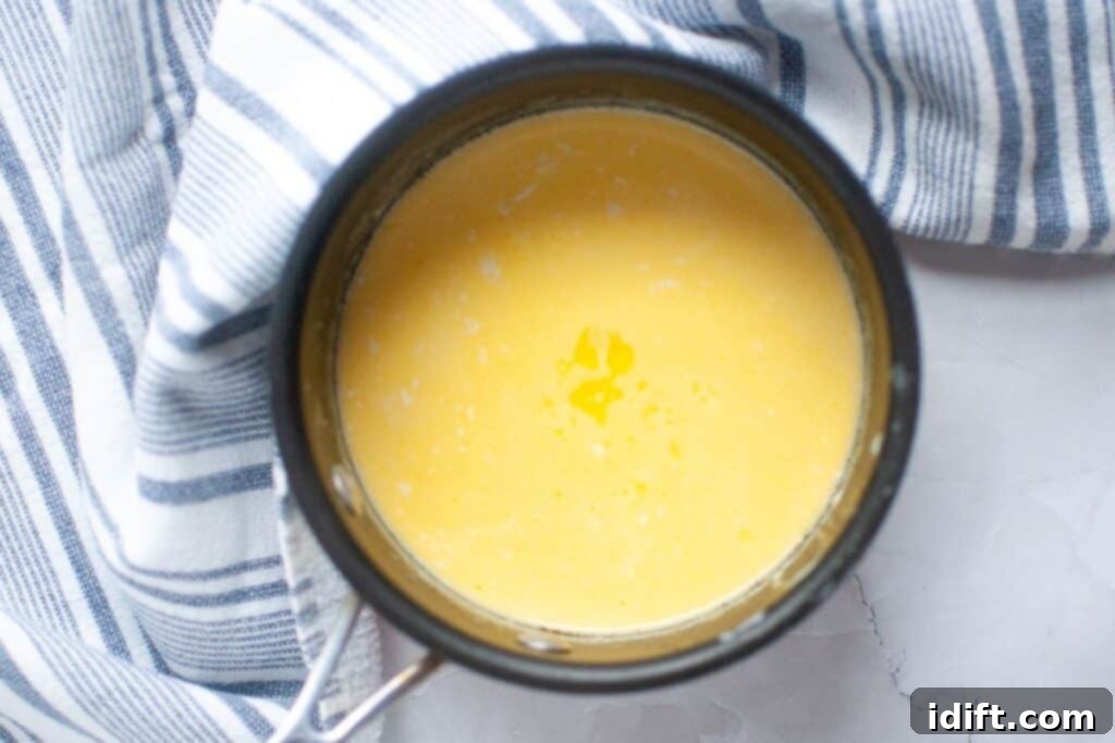 A pot of smooth yellow sauce or custard sits on a white surface next to a blue and white striped towel.