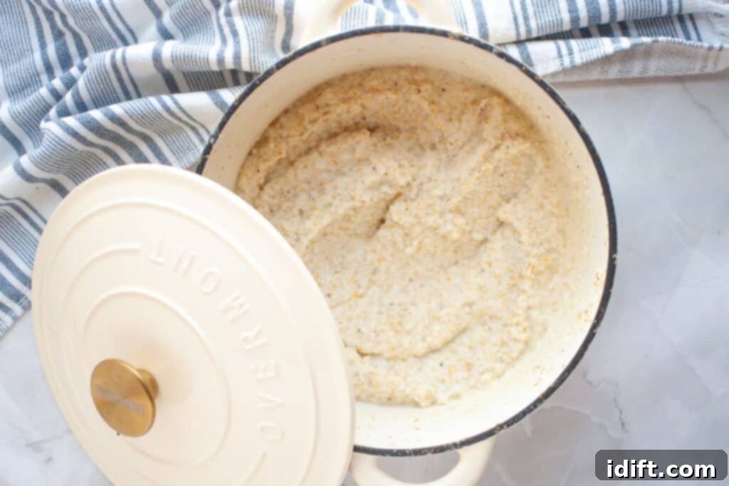 A pot of cooked oatmeal with the lid partially open sits on a marble countertop next to a blue and white striped cloth.