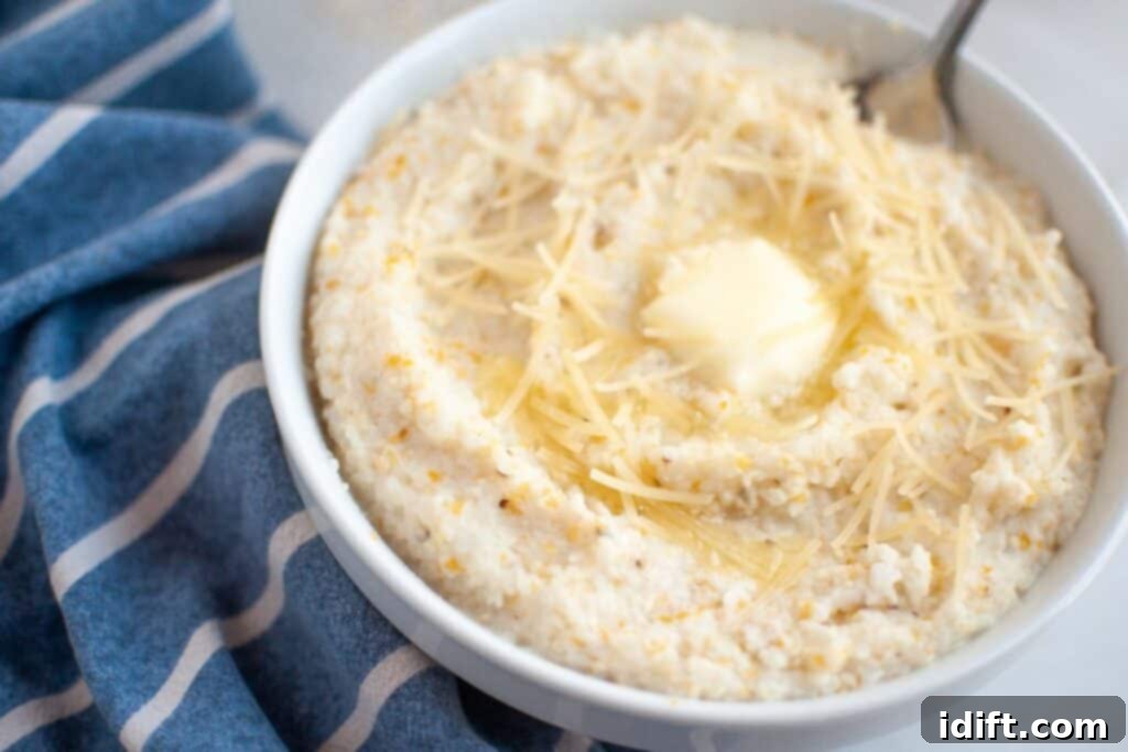 A bowl of creamy grits topped with shredded cheese and a pat of butter, with a spoon and a blue striped cloth nearby.