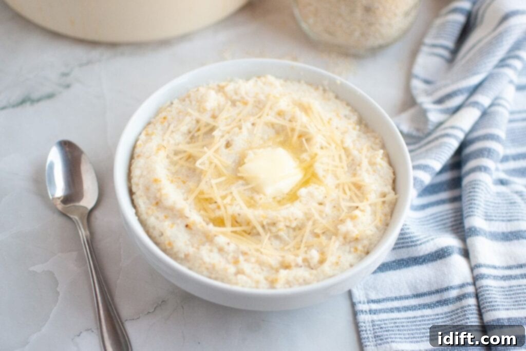 A bowl of grits topped with shredded cheese and a pat of butter, next to a spoon and a striped dish towel on a marble surface.