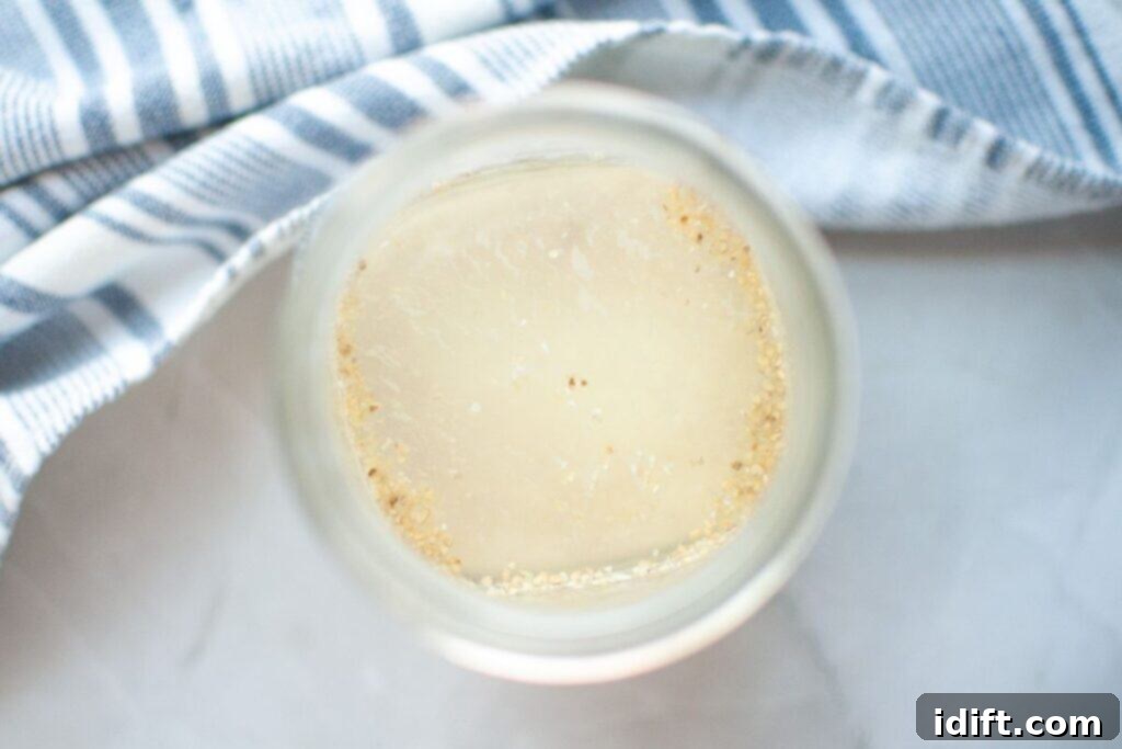 A glass jar with a cloudy liquid and sediment at the bottom, placed next to a blue and white striped cloth on a light surface.