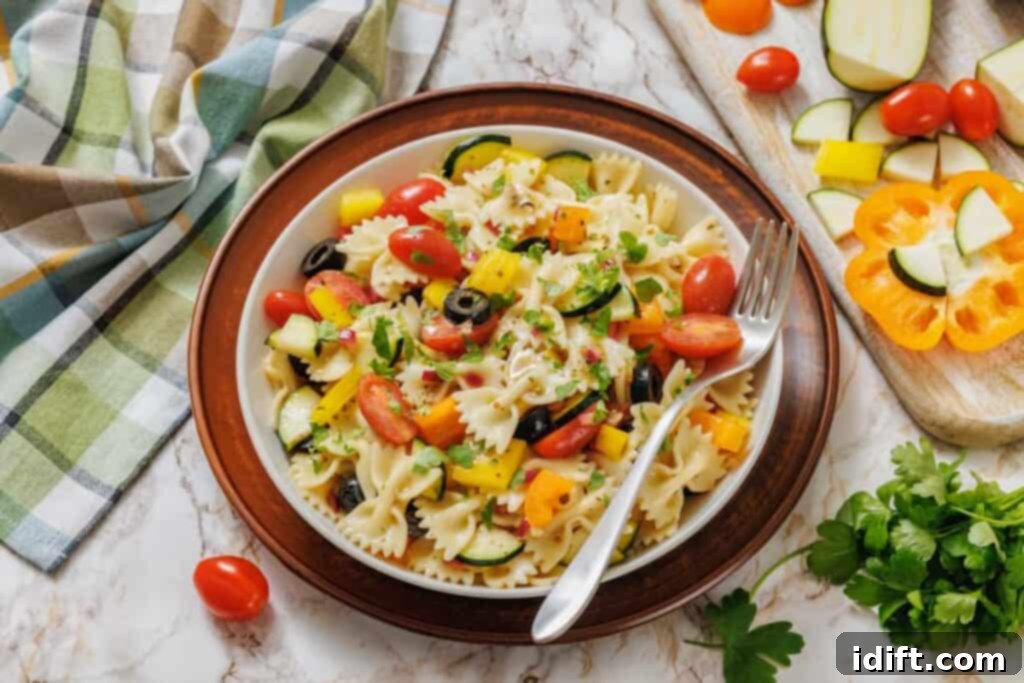 A plate of bowtie pasta salad with cherry tomatoes, black olives, zucchini, yellow bell pepper, and parsley on a marble surface, with a fork on the plate and vegetables nearby.