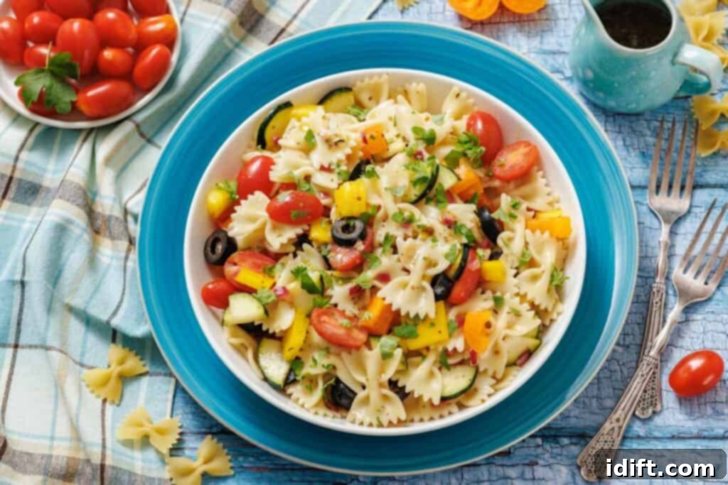 A bowl of bow-tie pasta salad with cherry tomatoes, black olives, yellow bell peppers, cucumbers, and herbs, placed on a blue plate with a fork and napkin nearby.