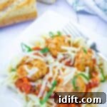 A plate of pasta topped with tomato sauce, meatballs, shredded cheese, and basil, served with a fork and a slice of bread in the background.