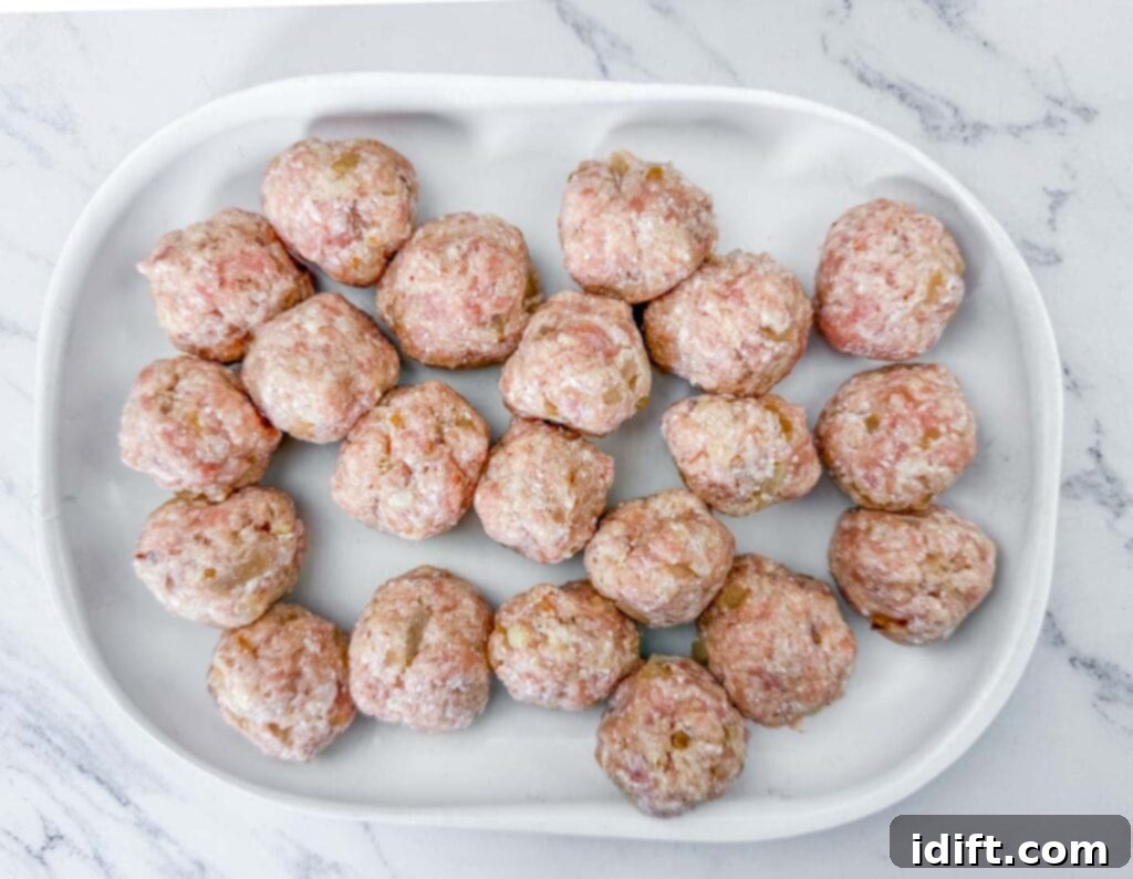 A white tray with raw meatballs arranged in rows on a marble surface.