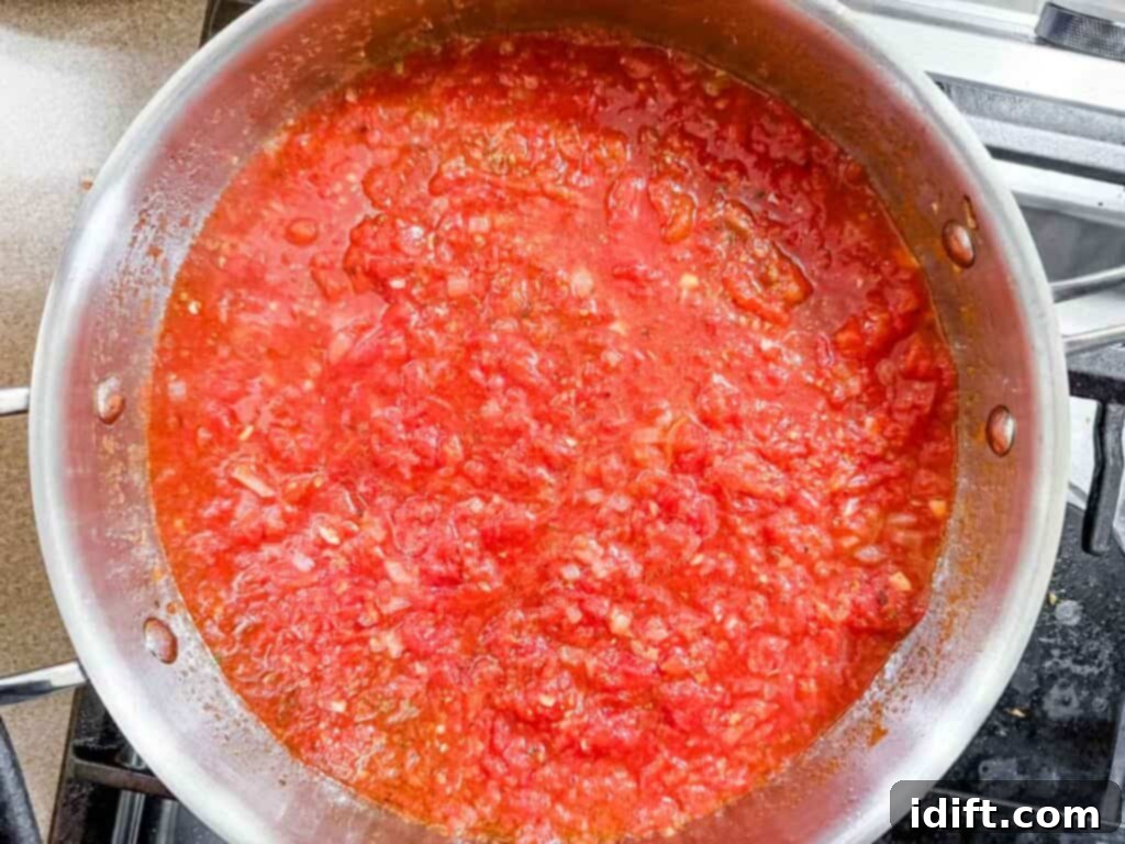 A stainless steel pan filled with simmering tomato sauce on a stovetop.