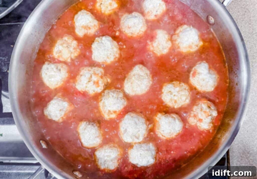 A pan of meatballs simmering in tomato sauce on a stovetop.