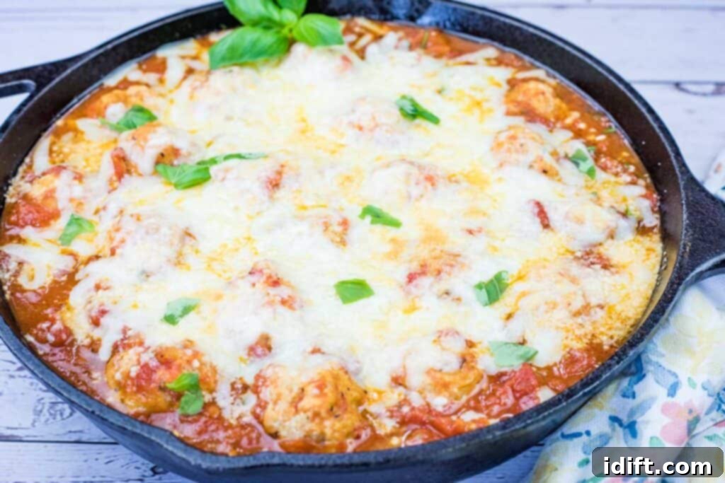 A cast iron skillet filled with baked meatballs in tomato sauce, topped with melted cheese and garnished with fresh basil leaves.