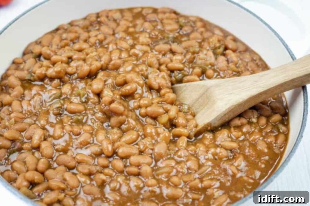 A pot of baked beans in sauce with a wooden spoon stirring them.