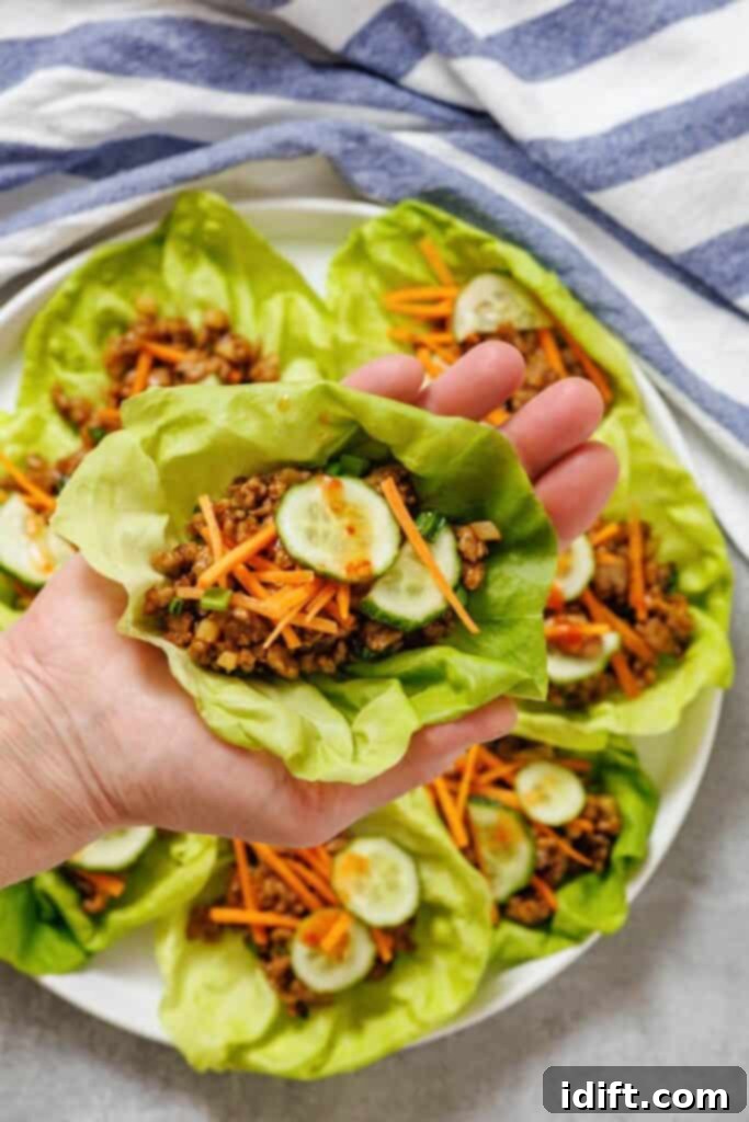 A hand holding lettuce cups filled with meat and vegetables.