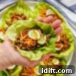A hand holding lettuce cups filled with meat and vegetables.