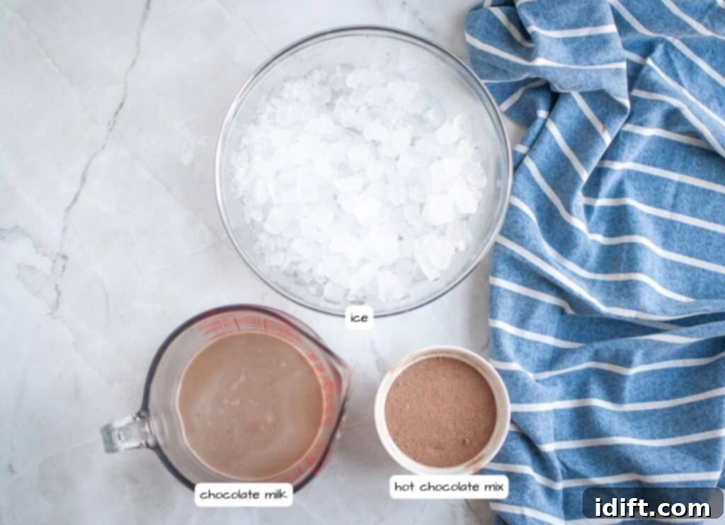 Frosty Chocolate Indulgence 4 Overhead shot of a white marble surface with a bowl of ice, a measuring cup of chocolate milk, and a small bowl of hot chocolate mix, all labeled, with a blue and white striped napkin to the side.