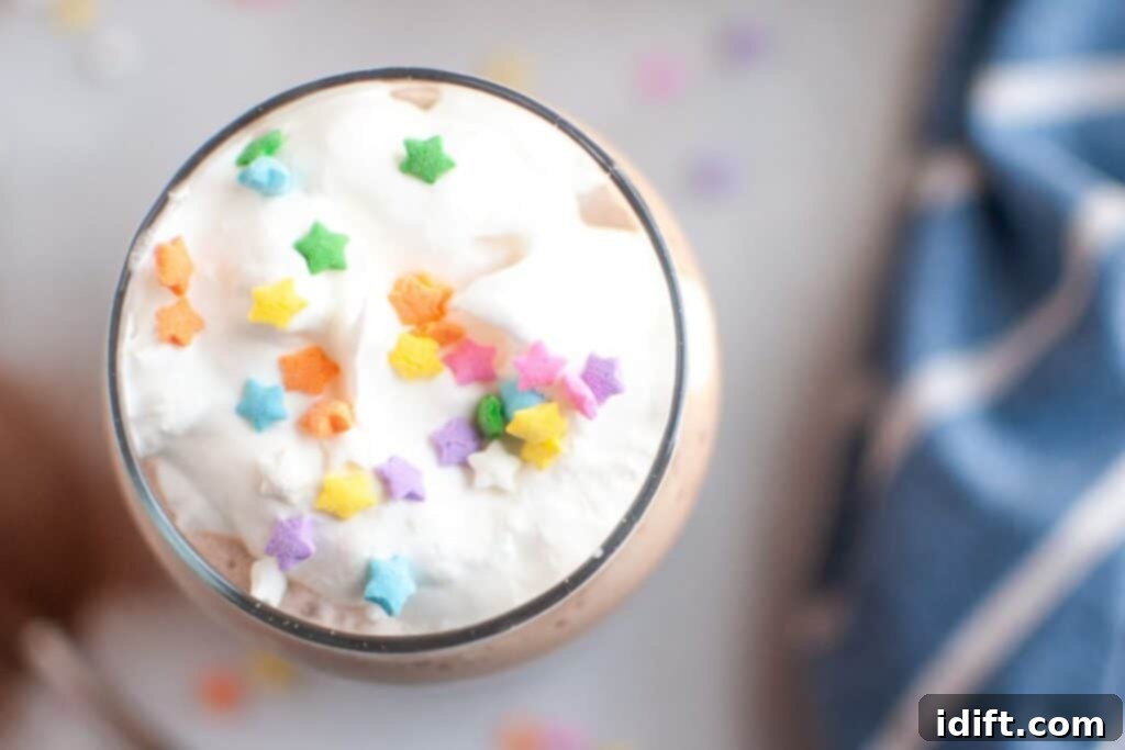 Frosty Chocolate Indulgence 7 A close-up, top-down shot of a clear glass filled with white whipped cream, generously topped with colorful star-shaped sprinkles, covering a light brown frozen hot chocolate.