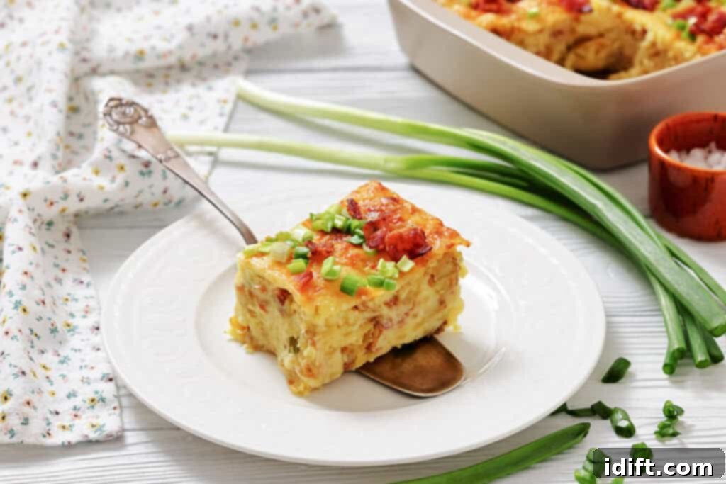 A slice of baked casserole topped with chopped green onions is served on a white plate with a spoon; green onions and a casserole dish are in the background.