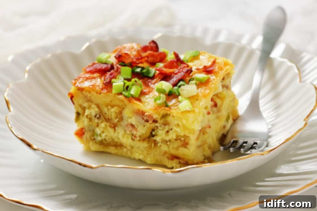 A slice of breakfast casserole topped with chopped green onions and bacon sits on a white plate with a fork.