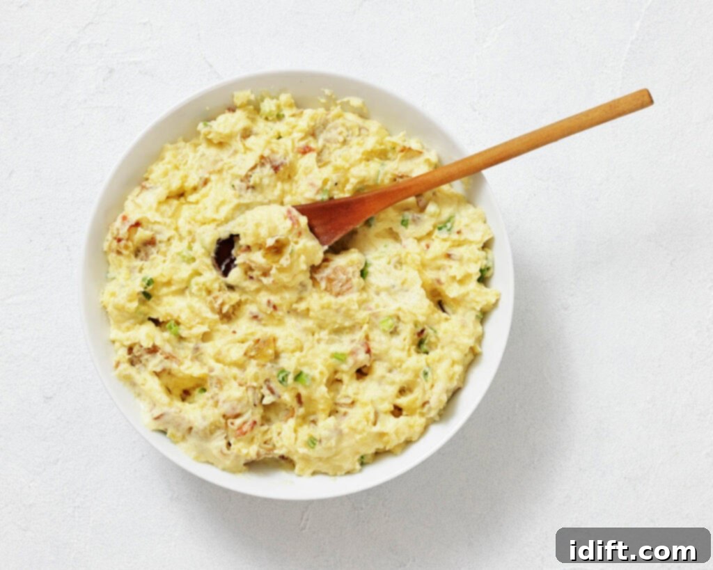 A bowl of potato salad with chopped herbs and a wooden spoon on a white surface.
