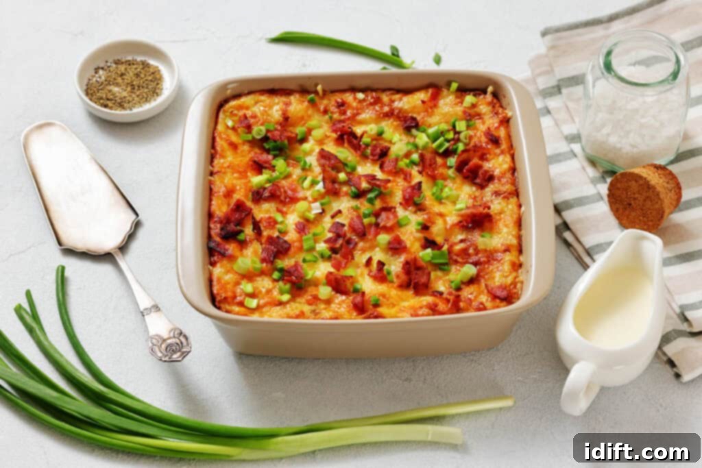 A baked casserole topped with chopped green onions and bacon bits, surrounded by fresh green onions, a dish of pepper, sea salt, bread, and a small jug of cream.