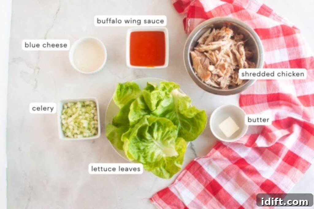 Ingredients for buffalo chicken lettuce wraps beautifully arranged on a kitchen counter: shredded chicken, a bottle of buffalo wing sauce, a bowl of crumbled blue cheese, chopped celery, fresh lettuce leaves, and a stick of butter, all accented by a festive red checkered cloth.