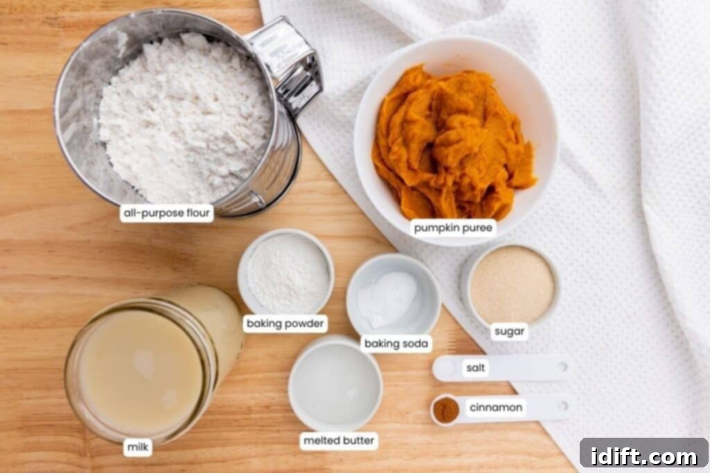 A top-down view of labeled baking ingredients in bowls and measuring spoons, including flour, pumpkin puree, milk, baking powder, baking soda, butter, sugar, salt, and cinnamon.
