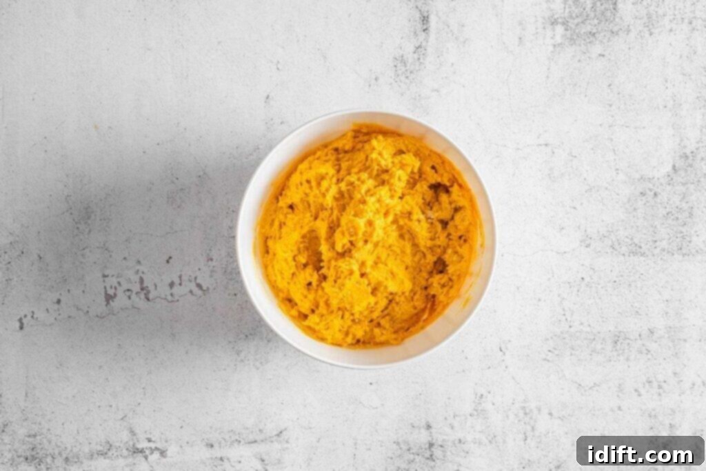 A white bowl filled with an orange dough is placed on a light textured surface.